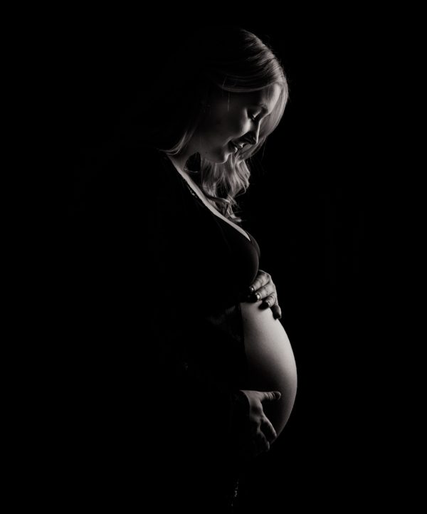 A woman standing in the dark holding her pregnant belly.